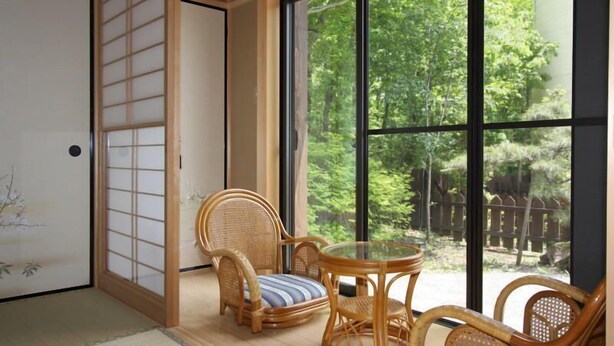 A traditional Japanese room with tatami flooring, a shoji screen, a tatami mat chair, a low wooden table, and a large window with a view of a forested area. - Suitaikyou (Nasu)