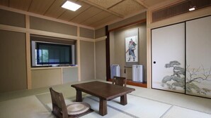 A traditional Japanese room with tatami flooring, a wooden table, chairs, a television, and a sliding door with a painting. - Suitaikyou (Nasu)
