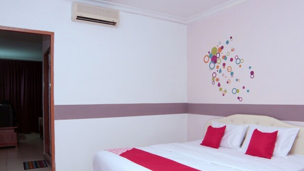A hotel room with a bed, a red and white bedspread, a wall with colorful circular decorations, and an air conditioning unit on the wall. - Super OYO 1173 Mandyrin Hotel (Sibu)