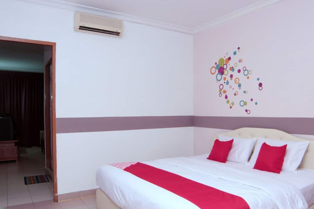 A hotel room with a bed, a red and white bedspread, a wall with colorful circular decorations, and an air conditioning unit on the wall.