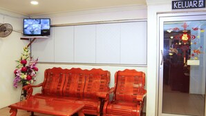 A reception area with a wooden sofa, a small table, a TV mounted on the wall, and a door with a sign reading "KELUAR". - Super OYO 1173 Mandyrin Hotel (Sibu)