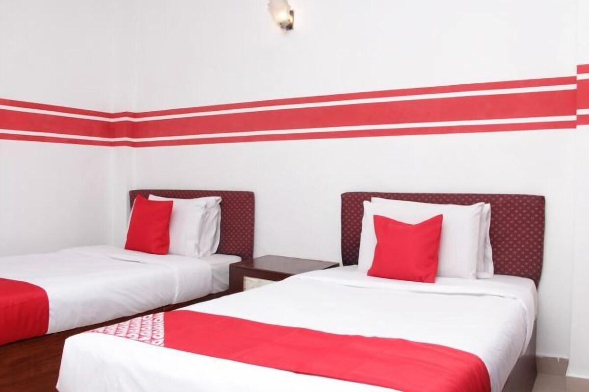 Habitación de hotel con dos camas, cada una con una colcha roja y blanca, un cabecero de madera y una mesita de noche pequeña.