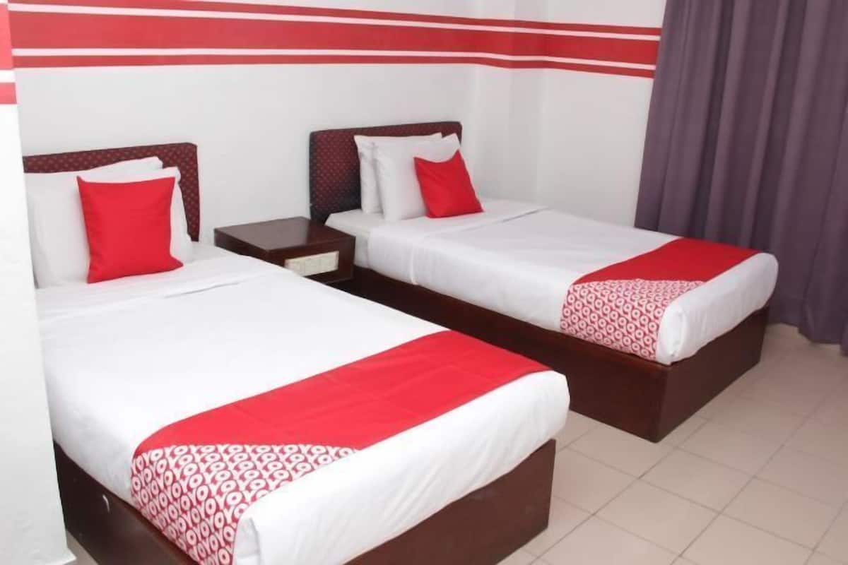 A hotel room with two beds, each with a red and white bedspread, a wooden headboard, and a nightstand.