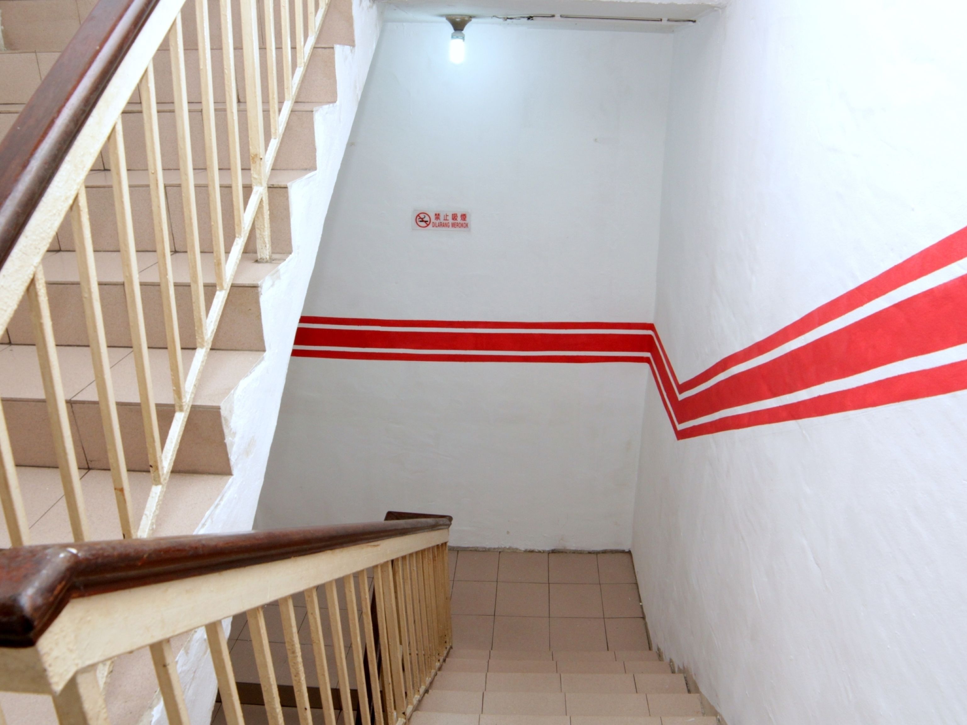 Una escalera con barandilla, una franja roja en la pared y un letrero de prohibido fumar.