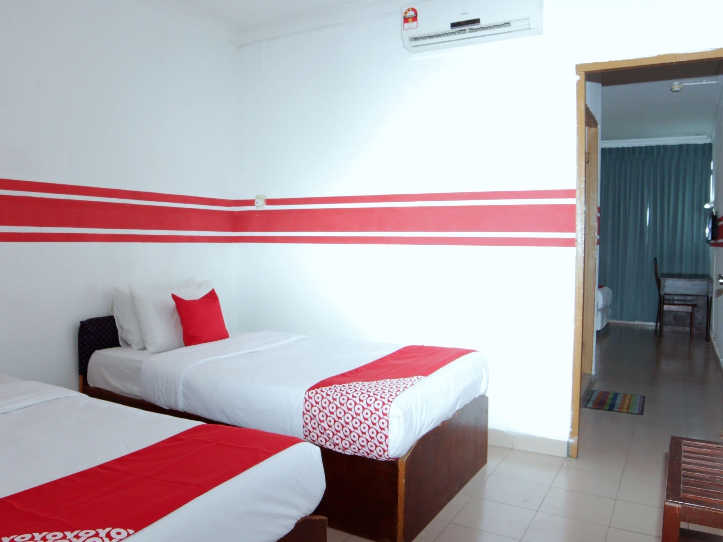 Habitación de hotel con dos camas, una pared a rayas rojas, una ventana y una puerta que da a un comedor.