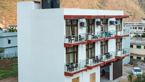 A multi-story hotel with balconies, air conditioning units, and a view of mountains in the background. - Hotel Tapovan Cottage (Narendranagar)