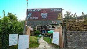 An entrance to a cafe with a signboard advertising open mic events and a contact number. - Hotel Tapovan Cottage (Narendranagar)