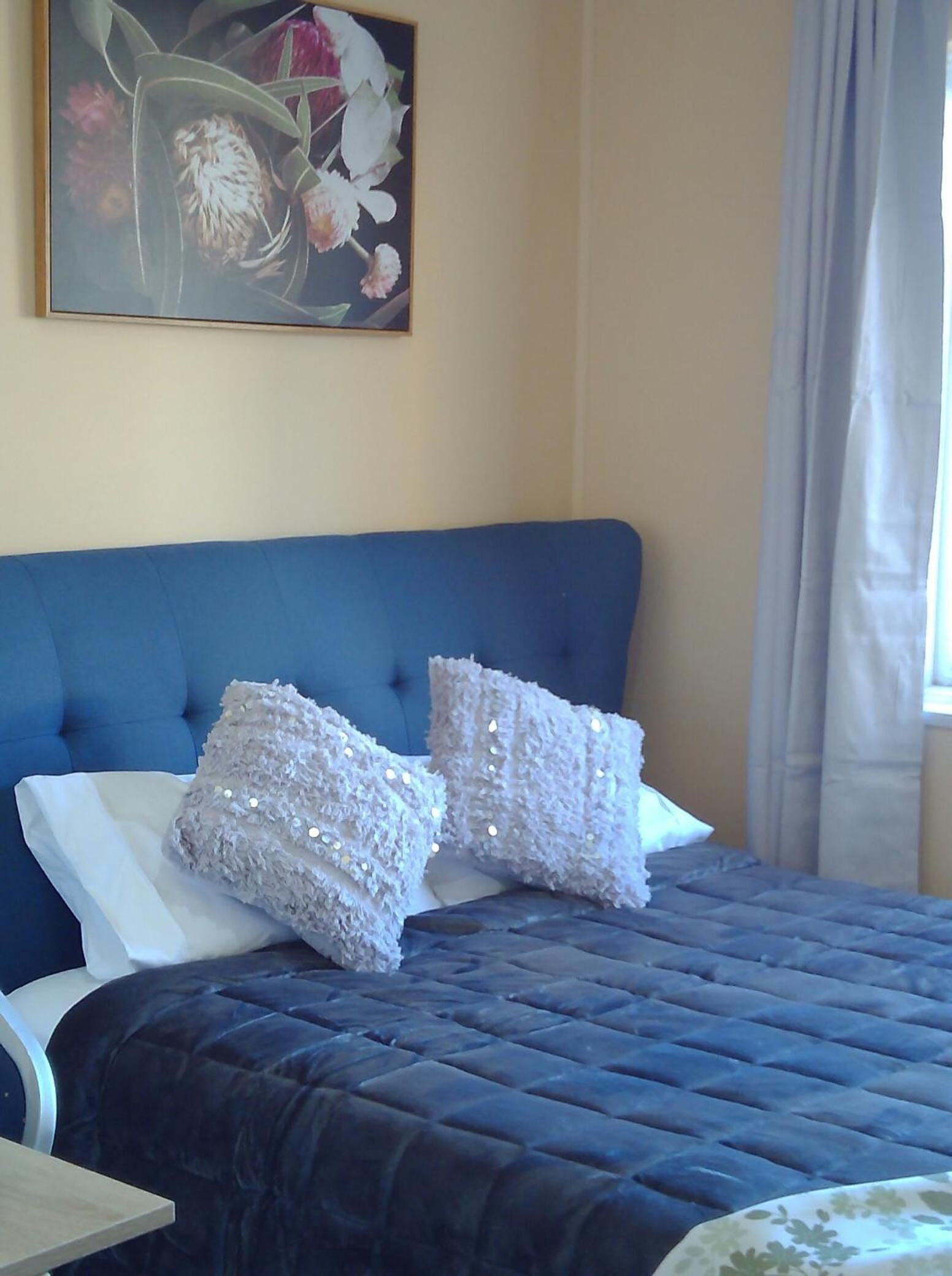 A bed with a blue headboard, two white pillows, and a quilted blue bedspread.