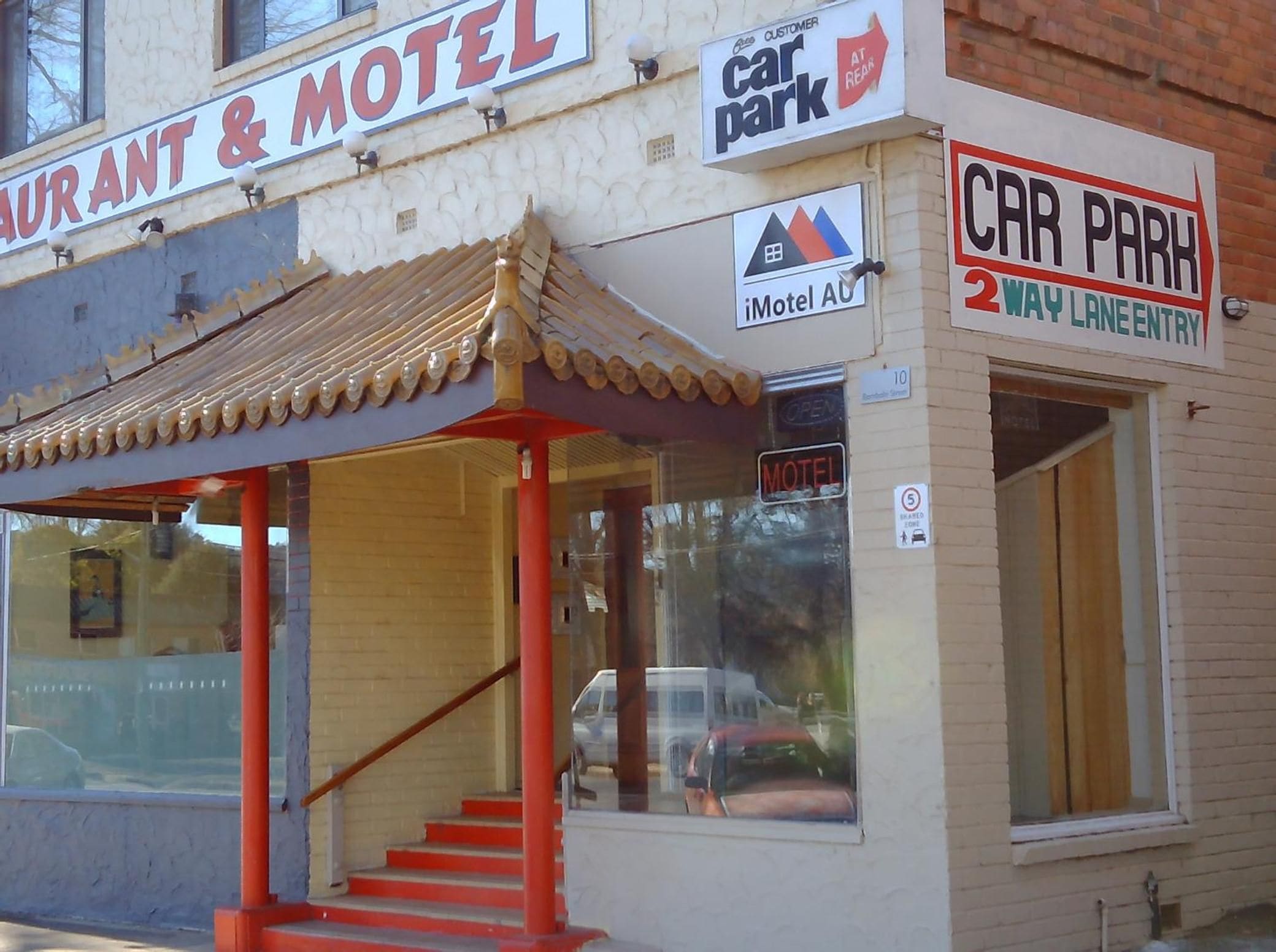 A building with a sign for a restaurant and motel, a car park, and a 2-way lane entry.