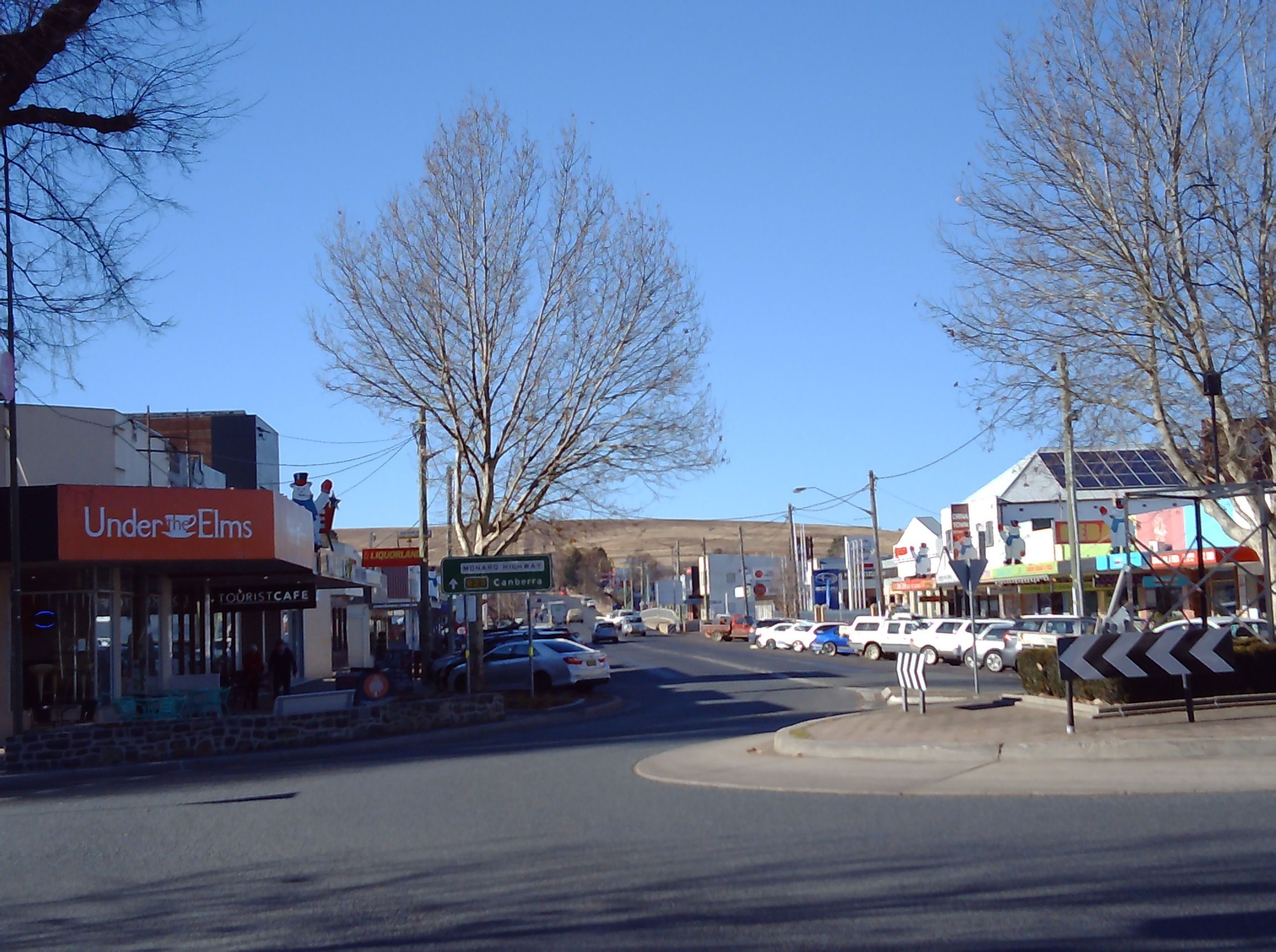 Une vue de rue avec un café appelé « Under the Elms » et un panneau indiquant « Monaco Highway ».