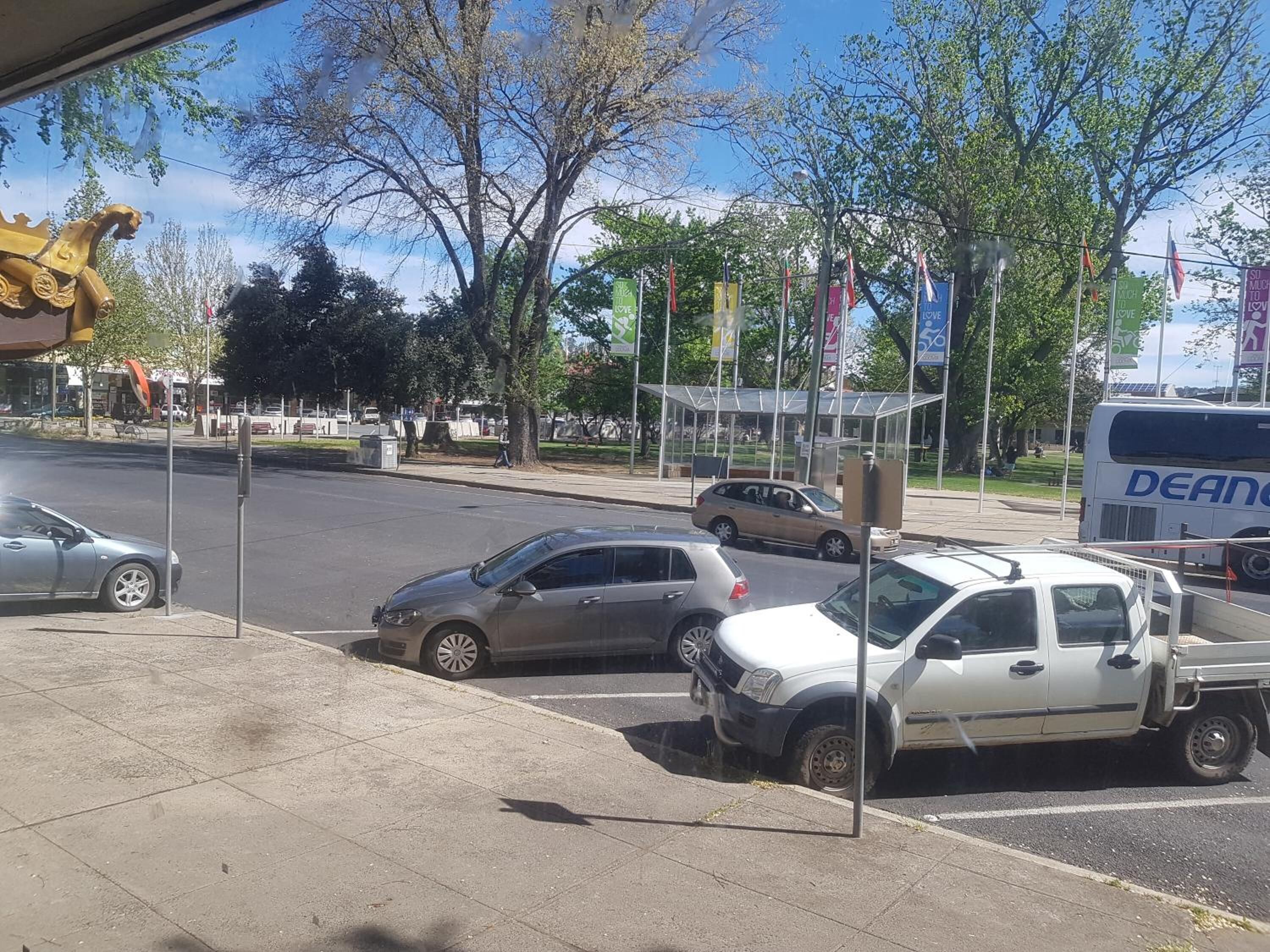 A parking lot with several cars and a bus, surrounded by trees and a bus shelter.