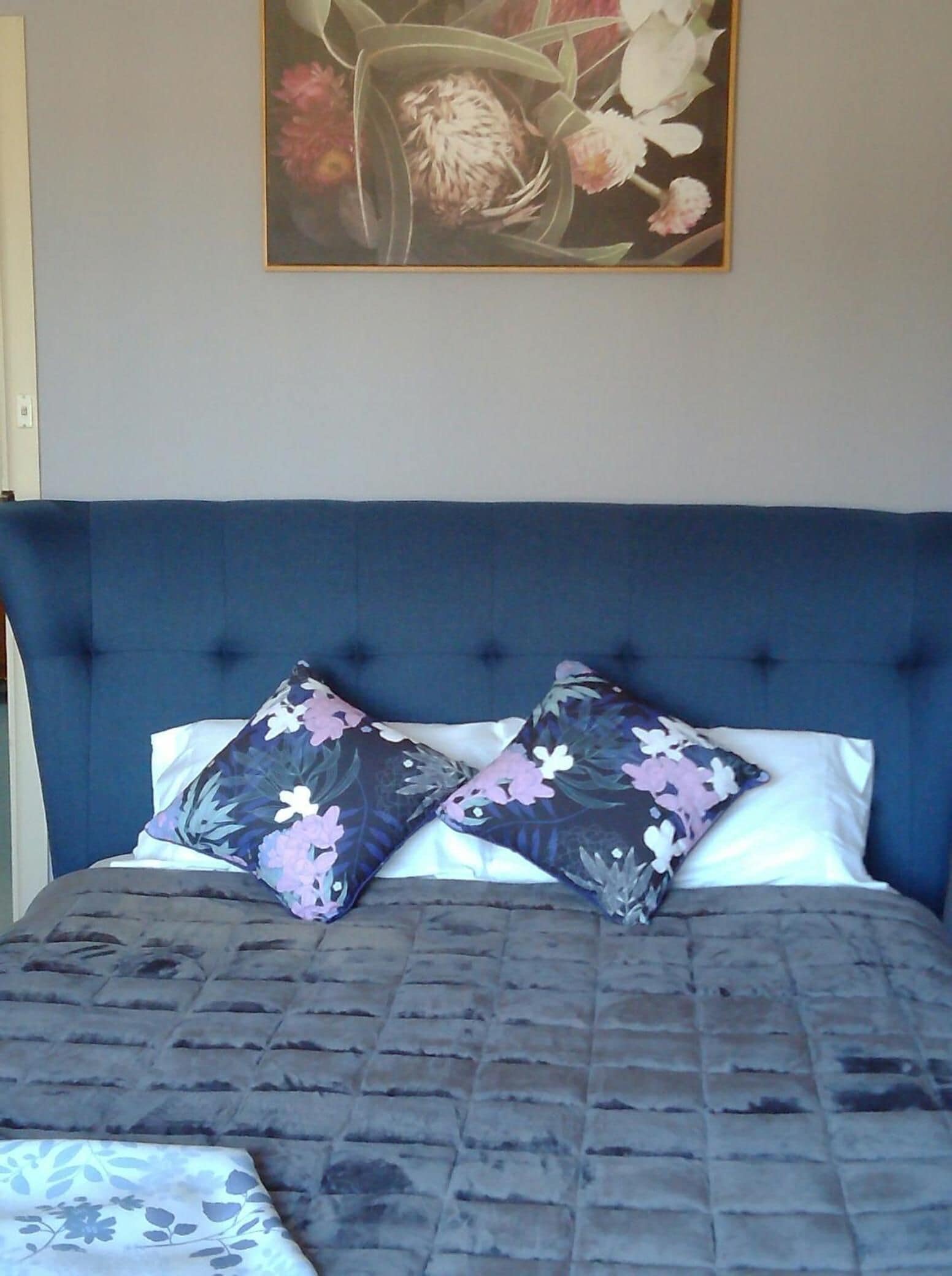 Un dormitorio con una cama grande, dos almohadas estampadas con flores y un cuadro de flores en la pared.