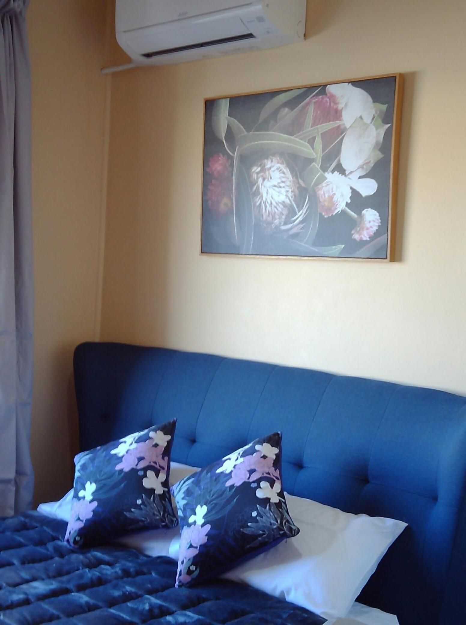 A room with a bed, a painting, and an air conditioning unit.