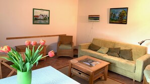 Un salón acogedor con un sofá verde, una mesa de centro de madera y un jarrón de tulipanes.