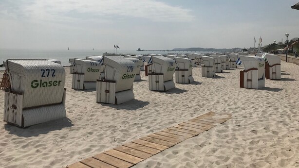Sillas de playa con la etiqueta 'Glaser' dispuestas en una playa arenosa, con un paseo de madera al frente.