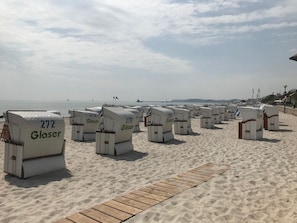 Beach chairs labeled "Glaser" arranged on a sandy beach with a wooden walkway in the foreground. - Apartment Haffkamp in Grömitz (Grömitz)