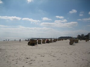 Ein Strand mit Sand und Fußabdrücken, ein Steg in der Ferne und einige Personen.