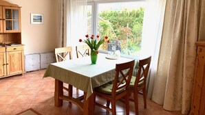 Un comedor con una mesa dispuesta para cuatro, sillas de madera, un florero verde con flores y vistas al exterior.