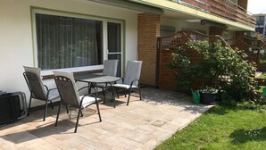 Un patio con una mesa y sillas, un pequeño jardín y un muro de ladrillo.