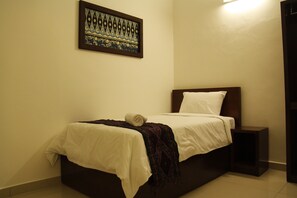 A neatly made bed with a white sheet and a dark blanket, a small bedside table, and a framed artwork on the wall.