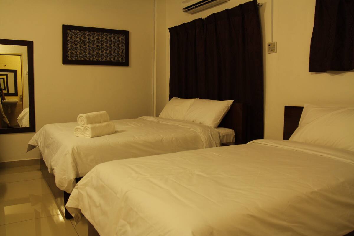 Une chambre d’hôtel avec deux lits, un miroir, un climatiseur fixé au mur et un tableau encadré.