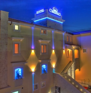 Un hotel con un letrero destacado que dice 'HOTEL' y la marca 'CENACOLO'. Cuenta con varias ventanas y una escalera que conduce a los pisos superiores.