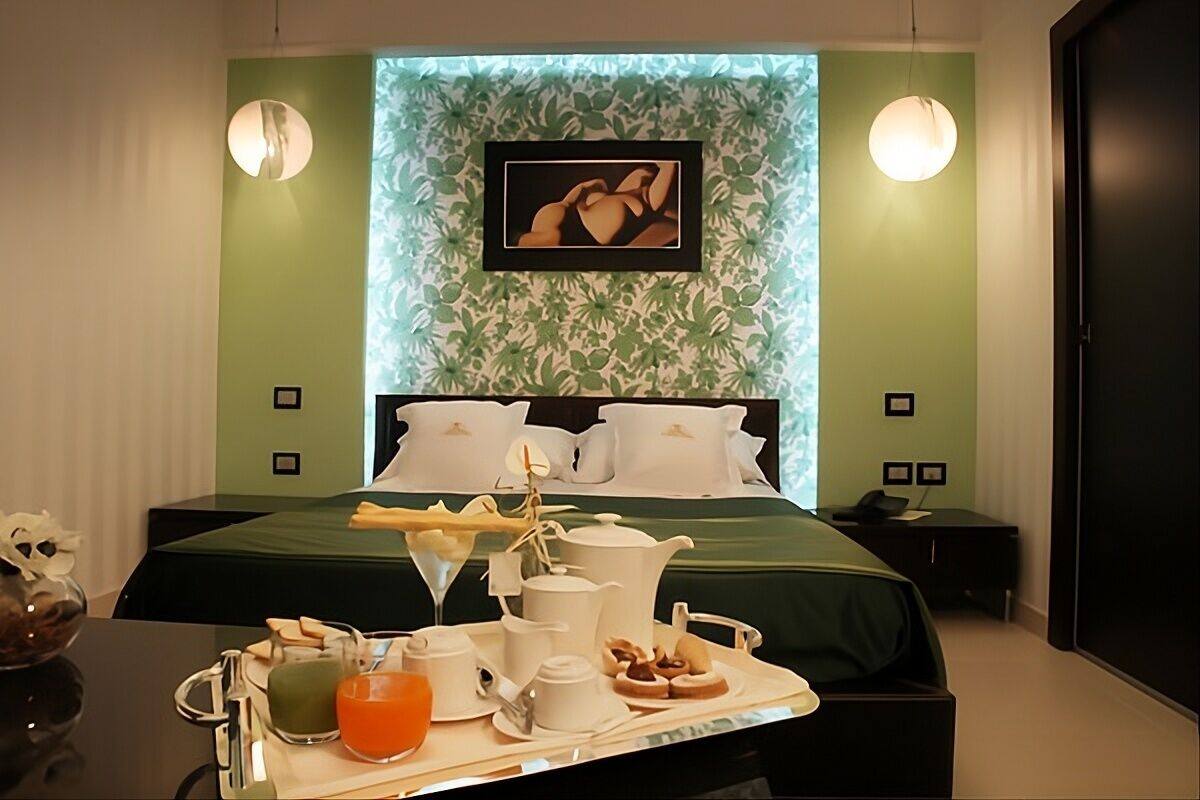 Una habitación de hotel con cama, mesitas de noche, una bandeja con alimentos para el desayuno y un cuadro en la pared.