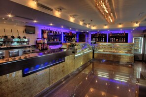Una zona de bar con una barra de mármol pulido, varias máquinas de café espresso y una vitrina con postres.