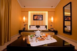 A hotel room with a neatly made bed, a dining table set with breakfast, and a large mirror on the wall.