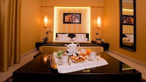 Habitación de hotel con una cama bien hecha, una mesa de comedor preparada para el desayuno y un espejo grande en la pared.