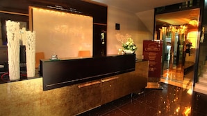Un mostrador de recepción de hotel con una mampara de vidrio, un letrero rojo y una araña.
