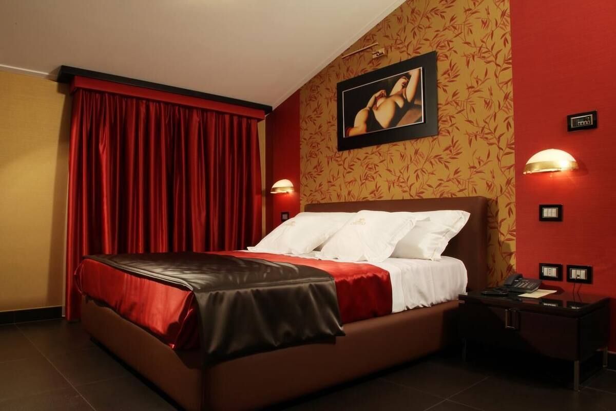 Una habitación de hotel con una cama grande, cortinas rojas, un cuadro colgado en la pared y una mesita de noche con teléfono.