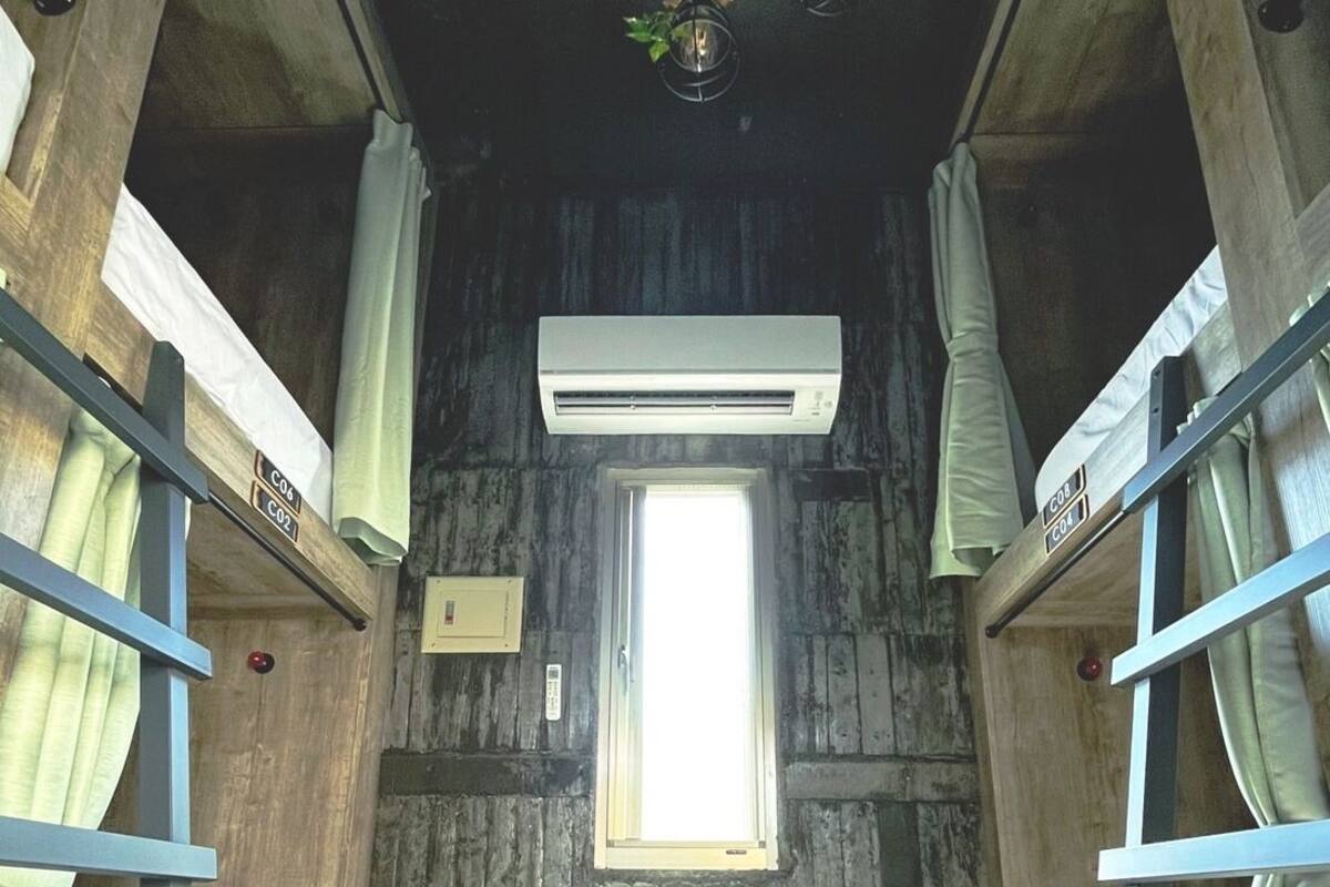 A bunk room with wooden walls, a window, bunk beds, and an air conditioning unit.