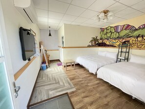 A hotel room with two beds, a mirror, a TV, a small table, a chair, a painting on the wall, and a ceiling fan.