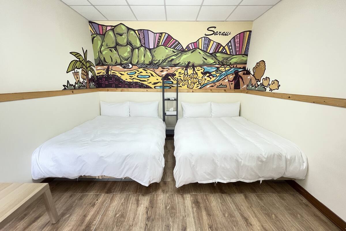 A room with two beds, a wooden floor, and a mural on the wall depicting a landscape with the word "Saraw".