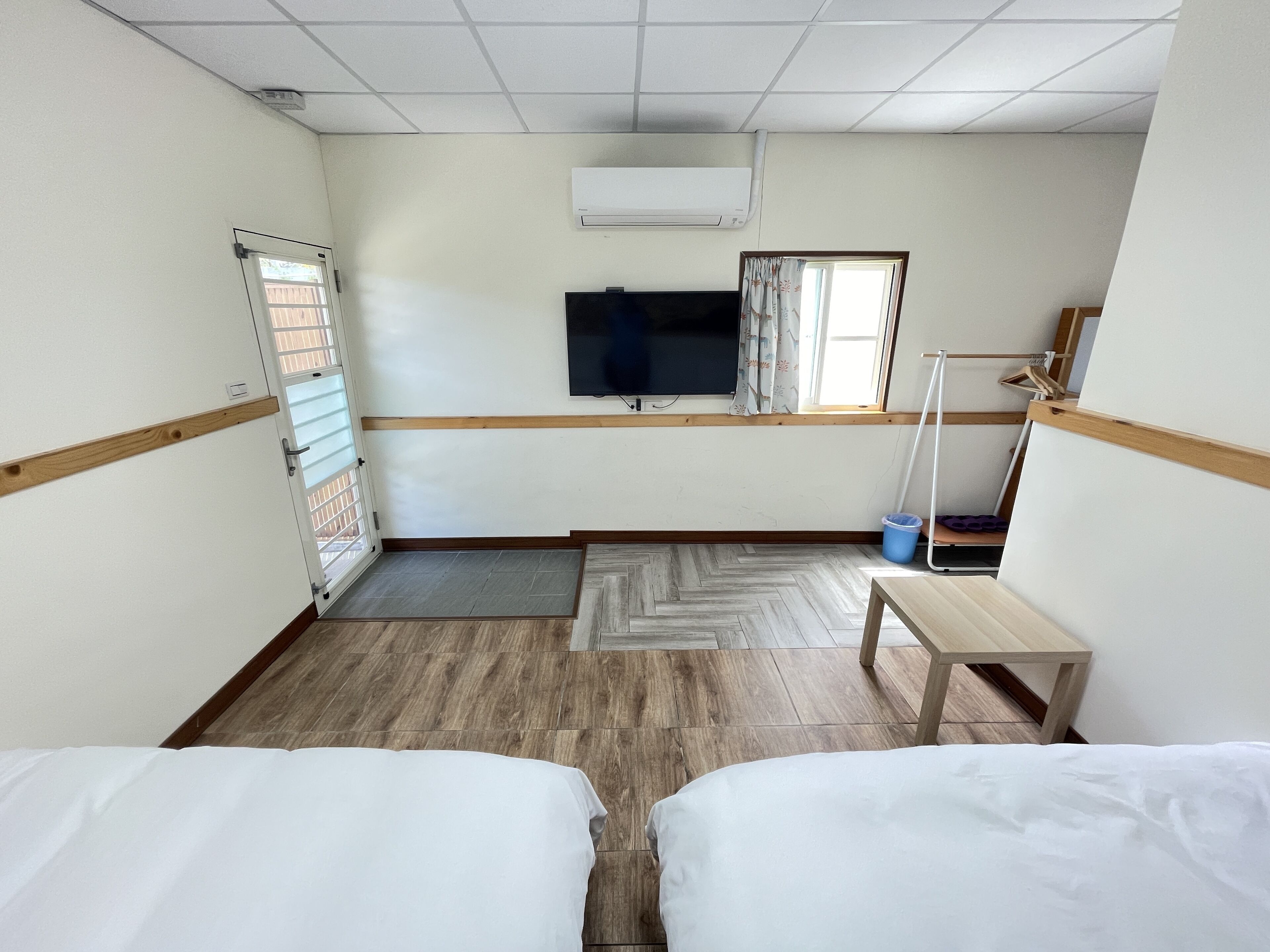 A hotel room with two beds, a TV, a window with curtains, a wooden floor, and a small table.