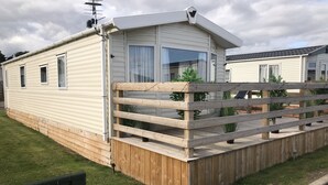 A mobile home with a wooden deck and a window with a curtain. - 2 bedroom modern caravan in Ladybank, 20 minutes to St Andrews (Ladybank)