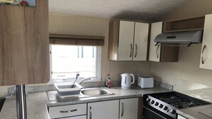 A compact kitchen with white cabinets, a stainless steel sink, a gas stove, and a toaster. - 2 bedroom modern caravan in Ladybank, 20 minutes to St Andrews (Ladybank)