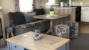 A compact living space with a sofa, a small table, a coffee table, and a kitchenette. - 2 bedroom modern caravan in Ladybank, 20 minutes to St Andrews (Ladybank)