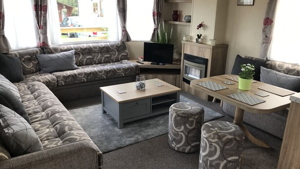 A living room with a sofa, a coffee table, a TV, a fireplace, and a dining table with chairs. - 2 bedroom modern caravan in Ladybank, 20 minutes to St Andrews (Ladybank)