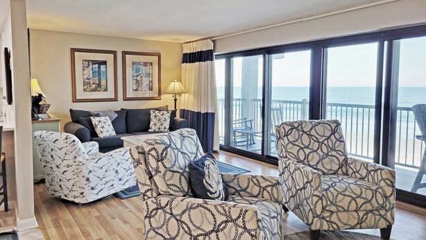 A spacious living room with a large window offering a view of the sea, a sofa set, patterned armchairs, and two framed artworks on the wall. - Oceanfront Condo on 7-Mile Beach, Elevator, Gated Peninsula Locale, Pools, Dock (Pawleys Island)