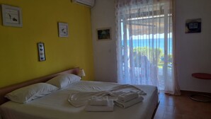 Une chambre d’hôtel avec un lit, une fenêtre ornée de rideaux légers et une vue sur la mer.