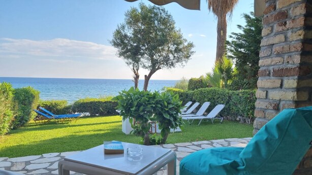 Une terrasse avec une table en pierre, un pouf bleu turquoise et une vue sur la mer.