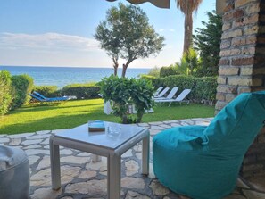 Une terrasse avec une table en pierre, un pouf bleu turquoise et une vue sur la mer.