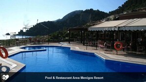Une piscine et un espace restaurant au Menigos Resort, avec une vue sur les montagnes en arrière-plan.