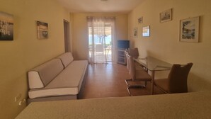 Un petit salon bien éclairé, comprenant un canapé, un téléviseur et une table à manger avec des chaises.