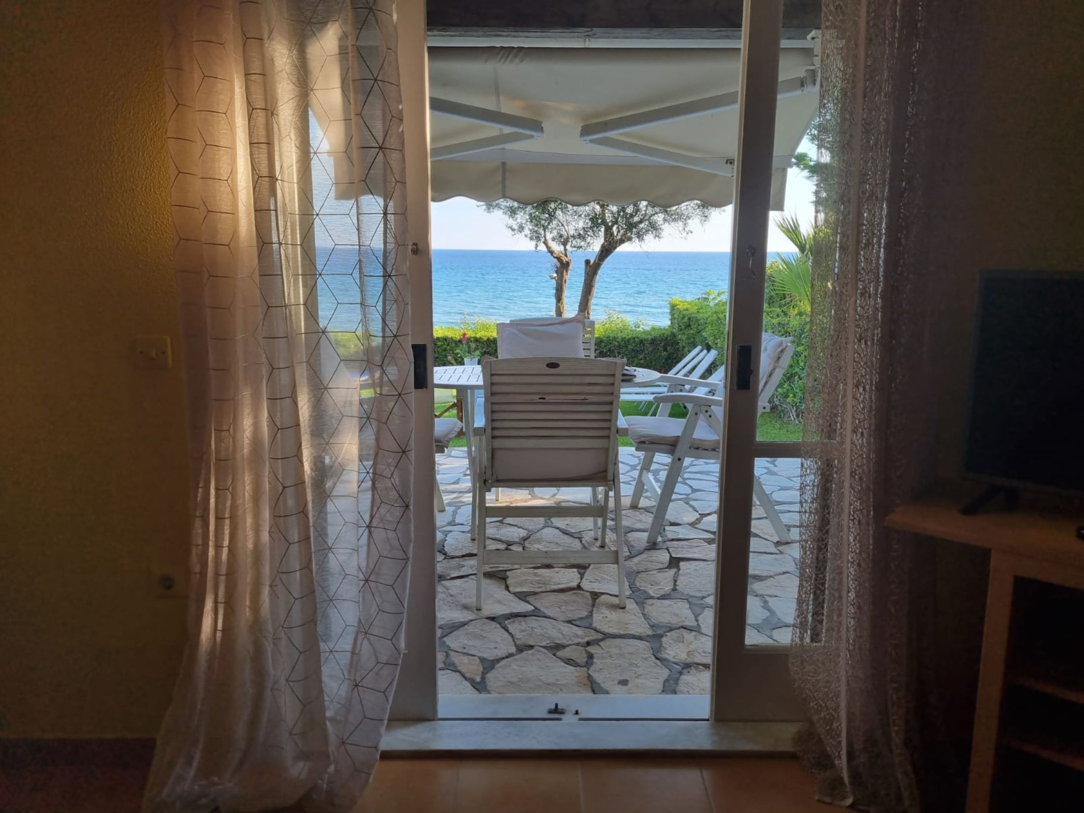 An open door leading to a patio with a table and chairs, a TV, and a view of the sea.