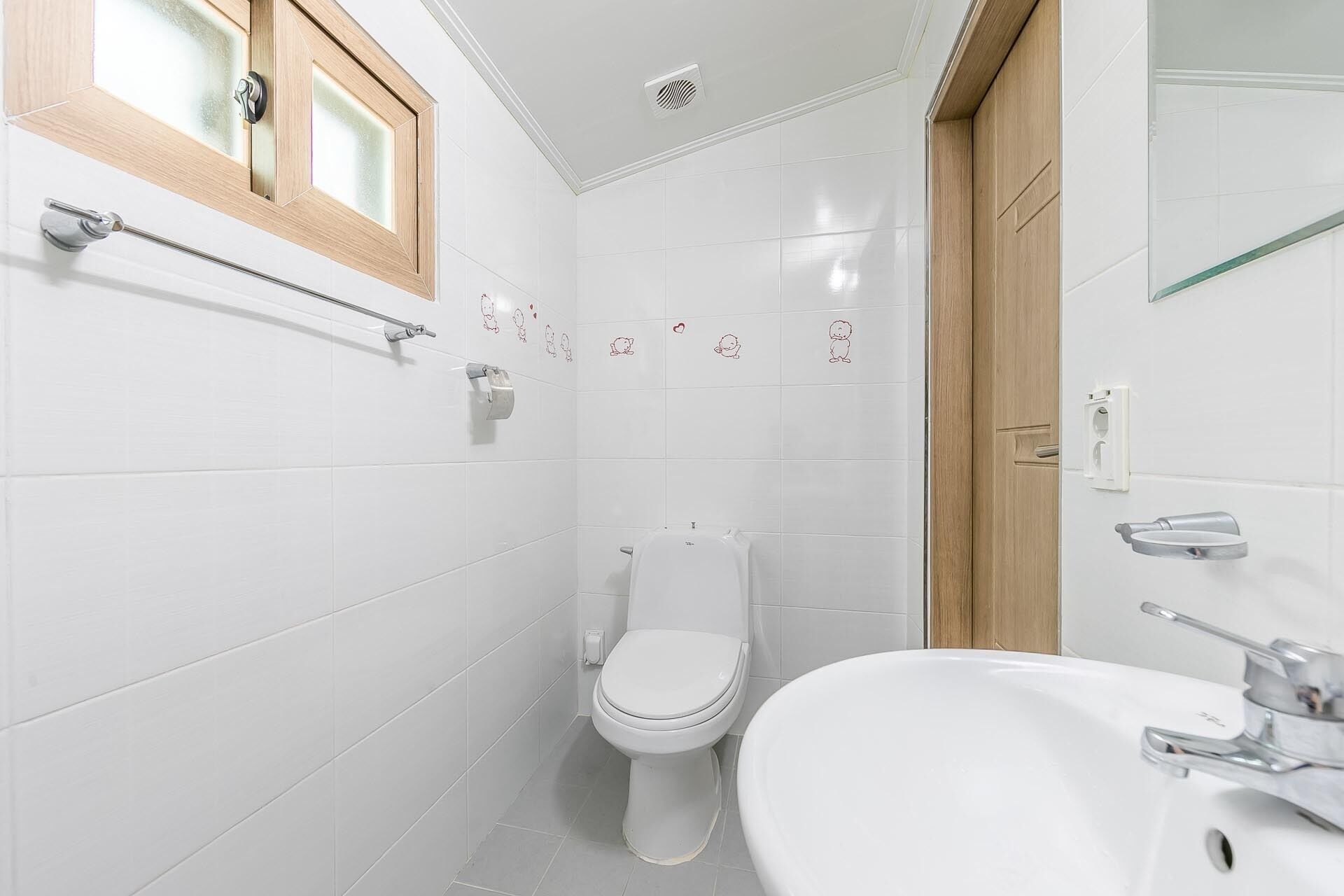 A bathroom with white tiles, a wooden-framed window, a toilet, a sink, and a towel rack.