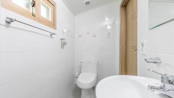 A bathroom with white tiles, a wooden-framed window, a toilet, a sink, and a towel rack.