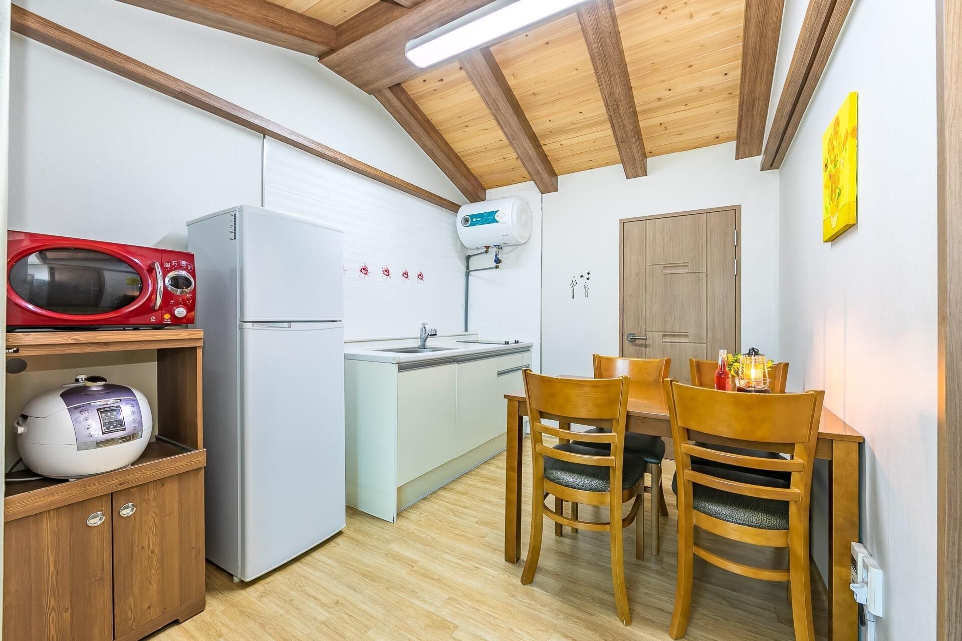 A compact kitchen with a microwave, refrigerator, and a water dispenser. There is a dining table with chairs and a wooden cabinet below.